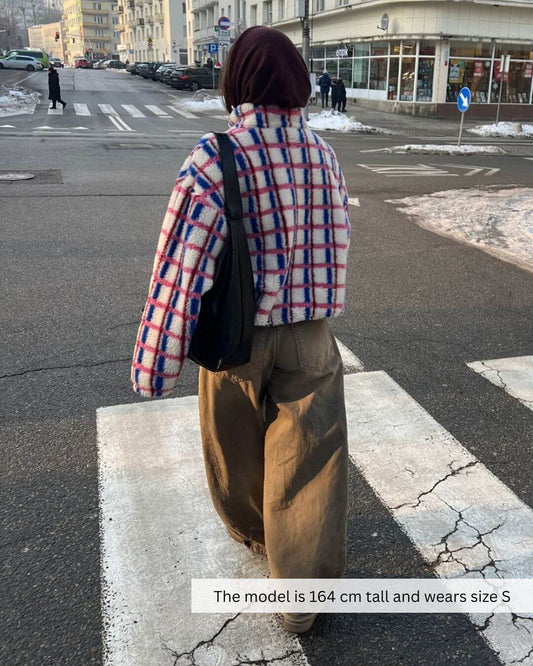 Model wearing an oversized 100% merino wool jacket in pink and cobalt color walking on a city street.