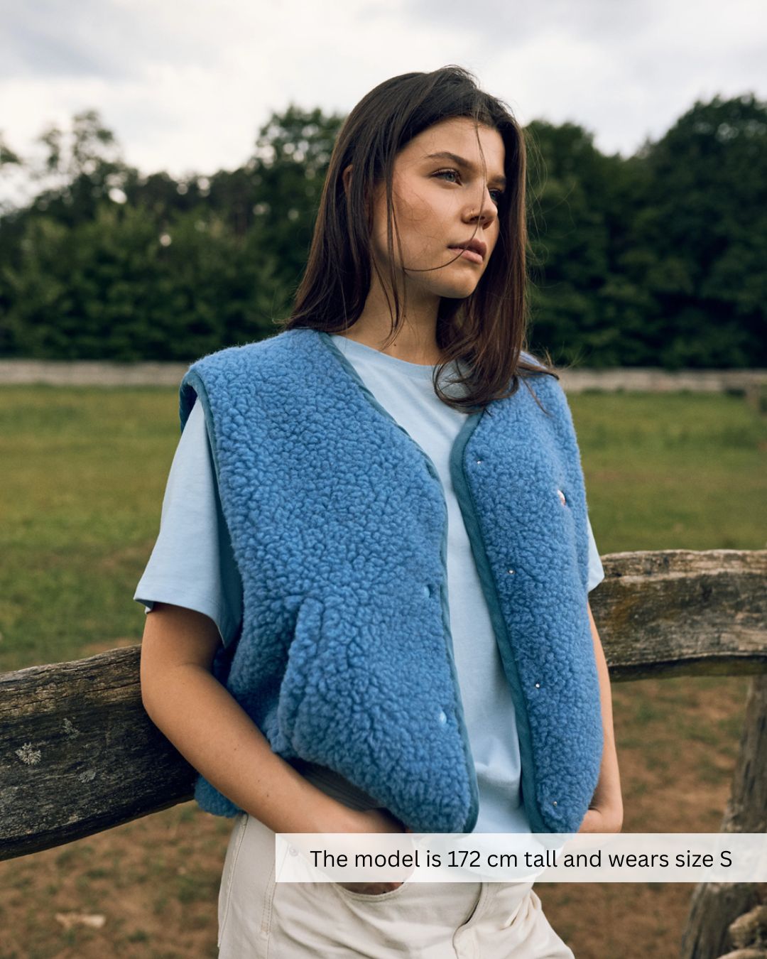 Woman sitting outdoors wearing a blue merino wool vest, natural merino wool vest for layering